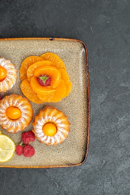 Vista superior deliciosos pasteles con rodajas de limón y mandarinas sobre un fondo oscuro galleta de frutas pastel de galletas de té dulce