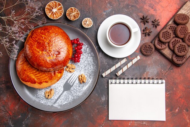 Vista superior de deliciosos pasteles con taza de té en la mesa oscura pastel de pastelería dulce