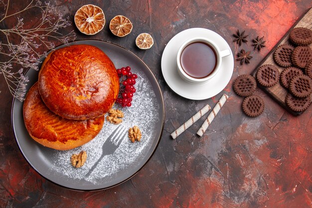 Vista superior de deliciosos pasteles con taza de té en la mesa oscura pasteles dulces pastel de pastelería