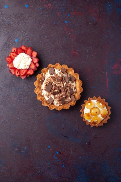Vista superior de deliciosos pasteles con trozos de crema y chocolate en la superficie oscura