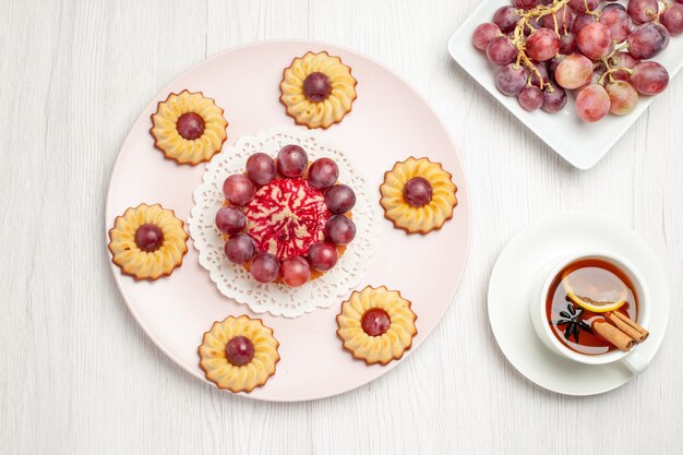 Vista superior deliciosos pasteles de uva con una taza de té en la mesa blanca postre galleta pastel de galletas