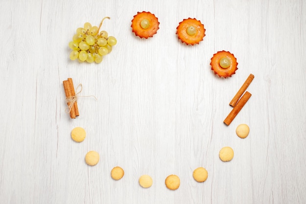 Vista superior de deliciosos pasteles con uvas y galletas en el escritorio blanco pastel de frutas galletas postre dulce té