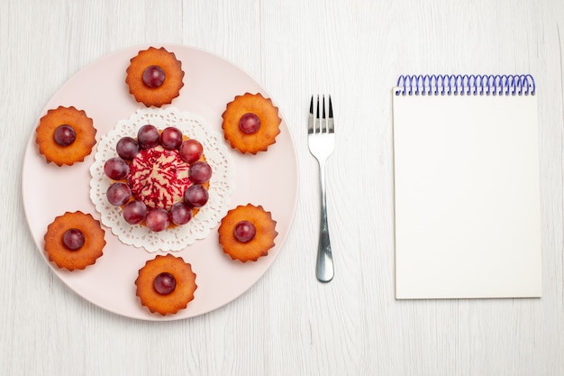 Vista superior de deliciosos pasteles con uvas en la tarta de postre de galletas de mesa blanca