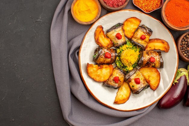 Vista superior deliciosos rollos de berenjena plato cocido con papas al horno y condimentos en el fondo oscuro plato de comida cocina de papa