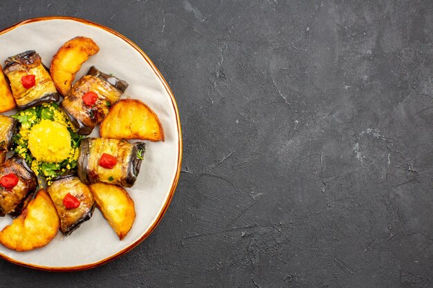 Vista superior deliciosos rollos de berenjena plato cocido con papas al horno en el piso oscuro plato de comida cocinar alimentos hornear papas fritas