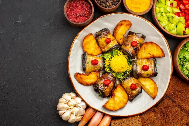 Vista superior deliciosos rollos de berenjena plato cocido con papas y hogazas de pan en el fondo oscuro cocinar alimentos freír plato hornear papa