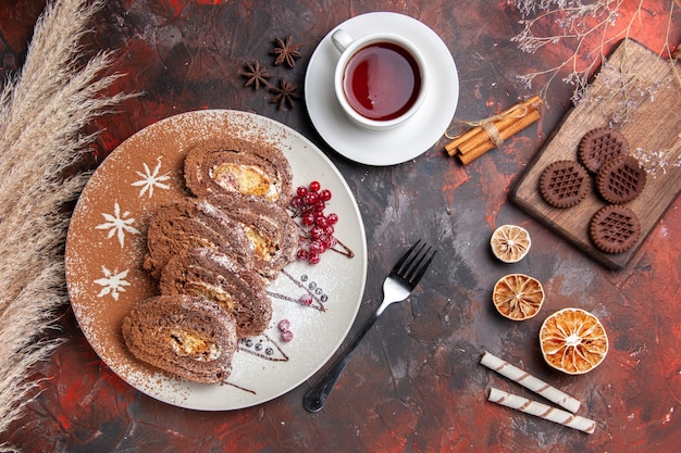 Vista superior de deliciosos rollos de galletas con galletas y té en un pastel de pastel dulce de mesa oscura