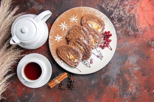 Vista superior de deliciosos rollos de galletas con una taza de té en el pastel de pastel dulce de mesa oscura