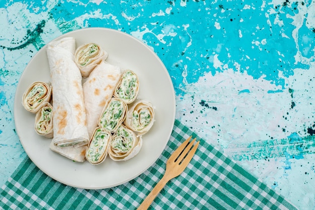 Vista superior de deliciosos rollos de vegetales enteros y cortados con una cuchara de madera en azul brillante, bocadillo de vegetales de rollo de comida