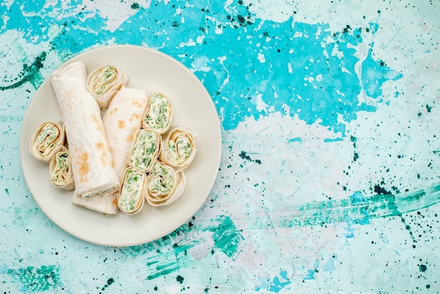 Vista superior de deliciosos rollos de vegetales enteros y en rodajas en un piso azul brillante, rollo de comida, bocadillo vegetal