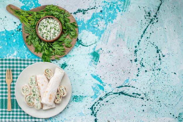 Vista superior de deliciosos rollos de vegetales enteros y en rodajas con verduras y ensalada en azul brillante, bocadillo de vegetales de rollo de comida