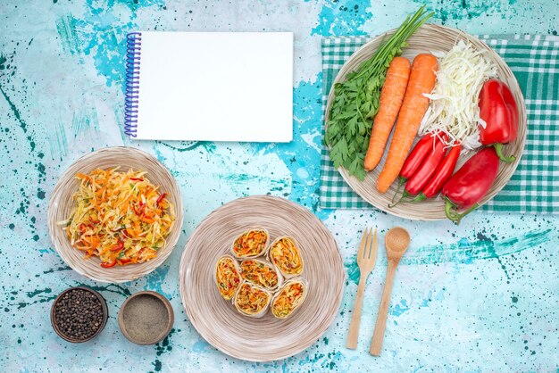 Vista superior de deliciosos rollos de verduras en rodajas junto con el bloc de notas de ensalada fresca y verduras en el escritorio azul brillante, rollo de ensalada de comida vegetal