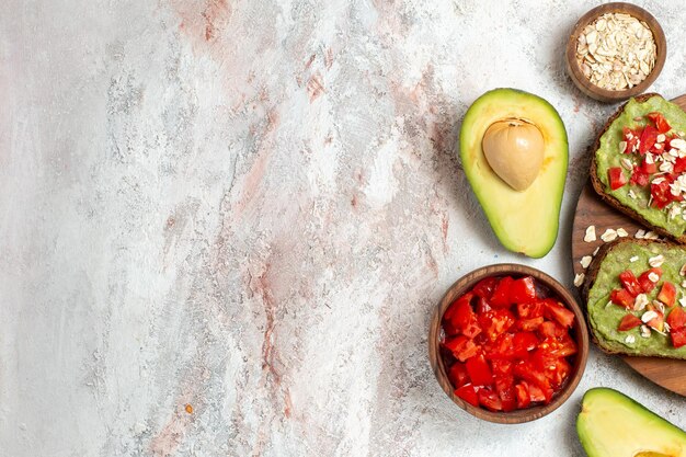 Vista superior de deliciosos sándwiches de aguacate con tomates rojos en rodajas sobre superficie blanca