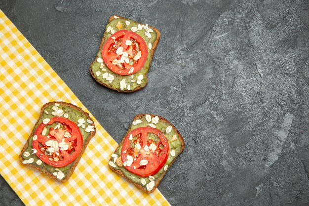 Vista superior deliciosos sándwiches útiles con pasta de aguacate y tomates en el bocadillo de pan de hamburguesa de sándwich de fondo gris