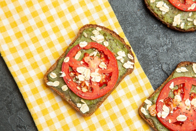 Foto gratuita vista superior deliciosos sándwiches útiles con pasta de aguacate y tomates en bocadillo de pan de hamburguesa sándwich de superficie gris