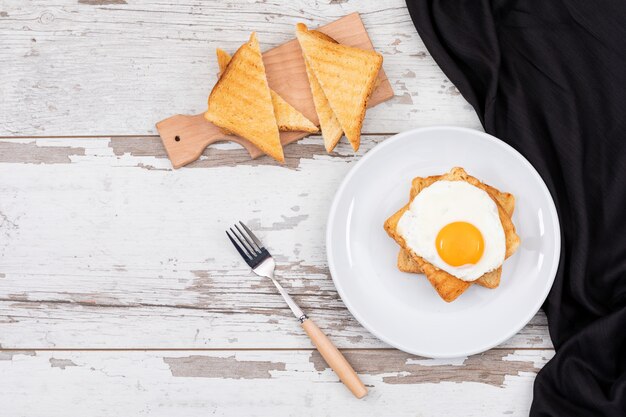 Vista superior del desayuno huevos fritos en un plato blanco con tostadas y copie el espacio en la superficie de madera horizontal