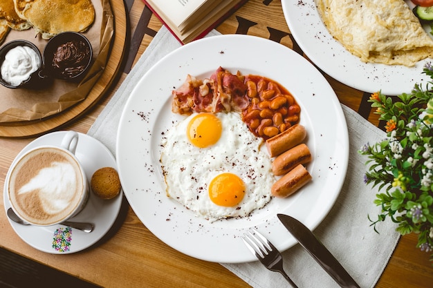 Vista superior desayuno inglés frito huevo frijoles salchichas tocino y taza de café sobre la mesa