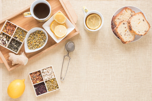 Vista superior de desayuno saludable con variedad de hierbas; limón; colador; un pan; jengibre e ingredientes