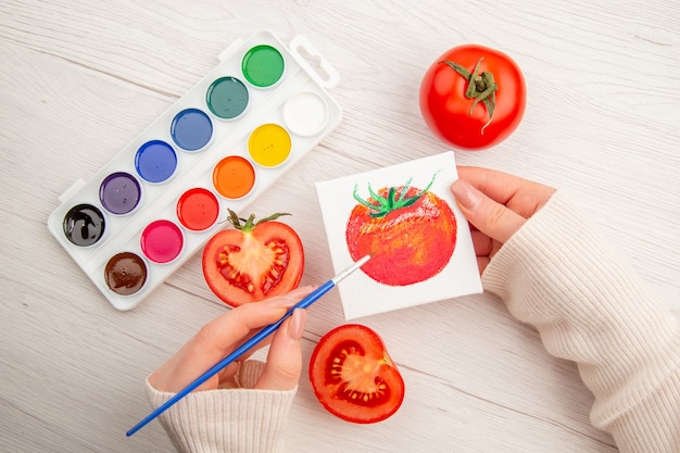 Vista superior dibujo de tomate pequeño con tomates y pinturas de colores sobre una mesa blanca