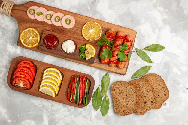Vista superior diferente composición de alimentos tomates limones salchichas pimientos con hogazas de pan en un escritorio blanco claro comida comida vegetal almuerzo foto