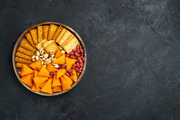 Vista superior de diferentes bocadillos, galletas, nueces y patatas fritas en la superficie gris oscuro