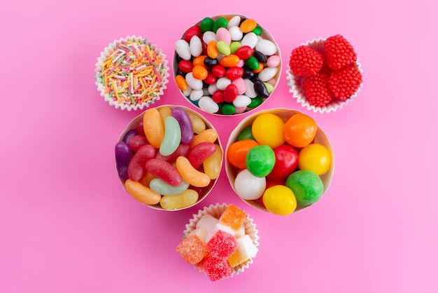 Una vista superior de diferentes caramelos coloridos dentro de pequeñas cestas en confitura de color rosa, azúcar dulce