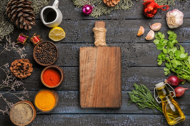 Vista superior de diferentes condimentos con aceite y verduras en piso oscuro