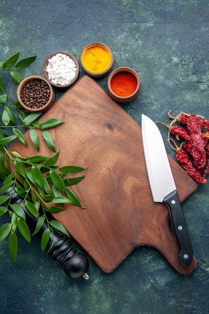 Foto gratuita vista superior de diferentes condimentos con escritorio de madera marrón en la superficie de color azul oscuro cubiertos de madera afilados árbol verde cocina