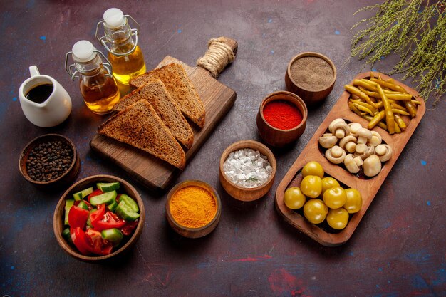 Vista superior de diferentes condimentos con panes de pan de verduras y aceite en el escritorio oscuro