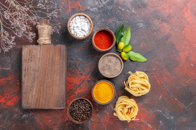 Vista superior de diferentes condimentos de pasta cruda en pasta de masa cruda de superficie oscura