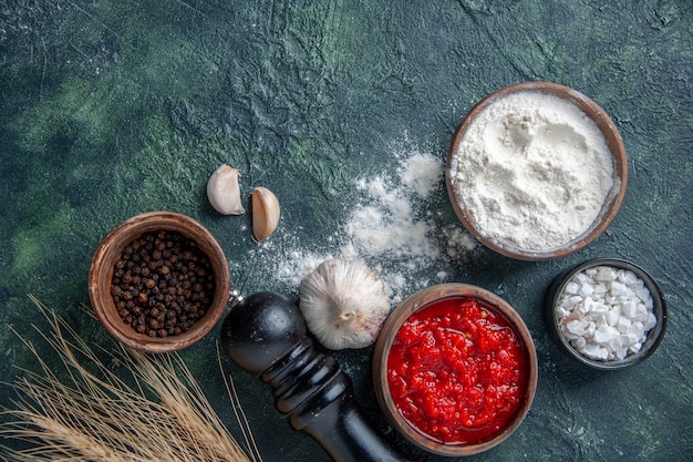 Foto gratuita vista superior de diferentes condimentos con salsa de tomate y harina sobre fondo oscuro ensalada de tomate maduro harina de masa de color vegetal