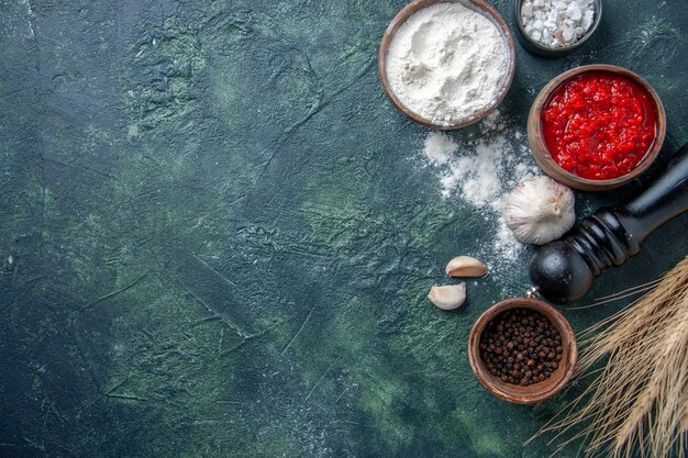 Vista superior de diferentes condimentos con salsa de tomate y harina sobre fondo oscuro ensalada de tomate maduro harina de masa de color vegetal