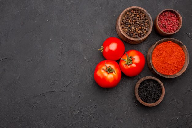 Vista superior de diferentes condimentos con tomates rojos frescos sobre fondo oscuro ensalada de comida condimento para la salud