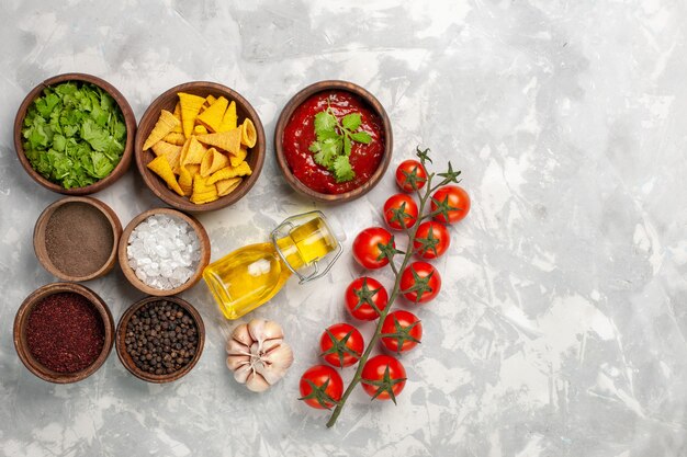 Vista superior de diferentes condimentos con tomates verdes y aceite en el escritorio blanco