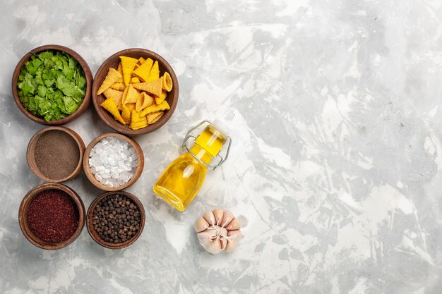 Vista superior de diferentes condimentos con verduras y aceite en el escritorio blanco