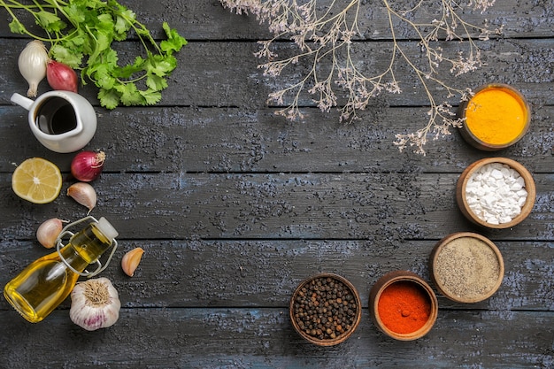 Vista superior de diferentes condimentos con verduras en el escritorio oscuro