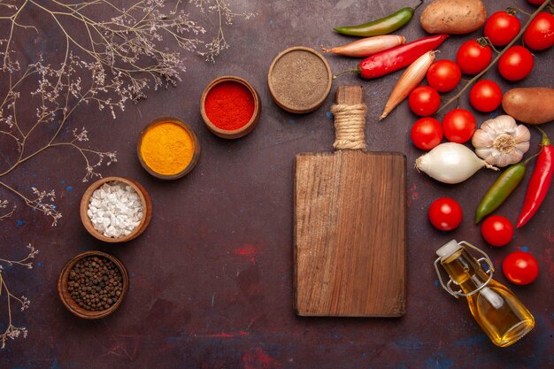 Vista superior de diferentes condimentos con verduras frescas en el espacio oscuro