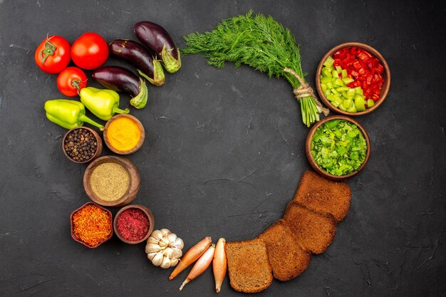 Vista superior de diferentes condimentos con verduras y hogazas de pan oscuro en el escritorio oscuro, condimentos para ensaladas, pan, alimentos saludables