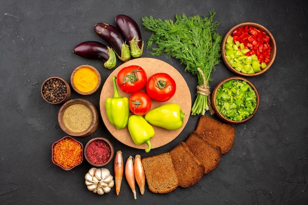 Vista superior de diferentes condimentos con verduras y hogazas de pan oscuro sobre el fondo oscuro, condimentos para ensaladas, pan, alimentos saludables