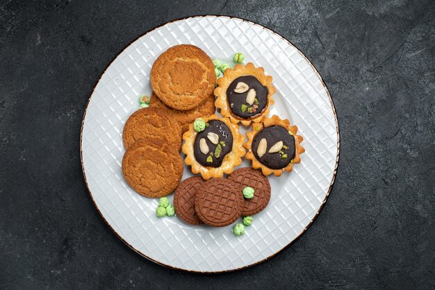 Vista superior de diferentes cookies galletas dulces y deliciosas dentro de la superficie gris