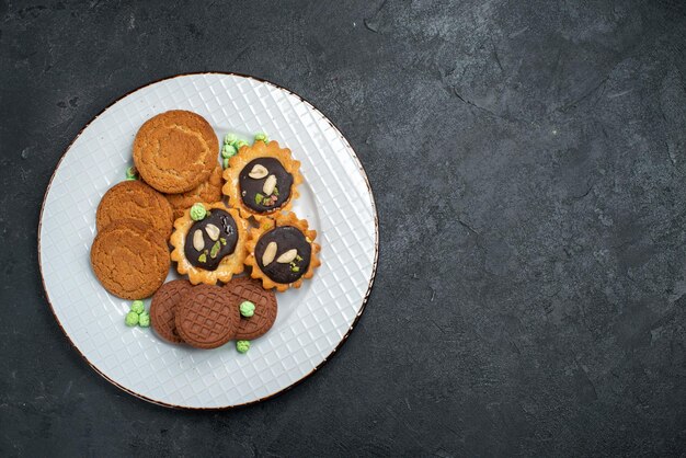 Vista superior de diferentes cookies galletas dulces y deliciosas dentro de la superficie gris