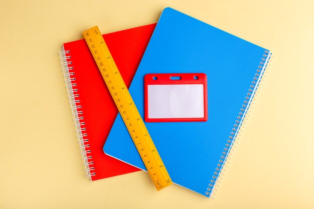 Vista superior de diferentes cuadernos azul y rojo con regla sobre superficie amarilla clara