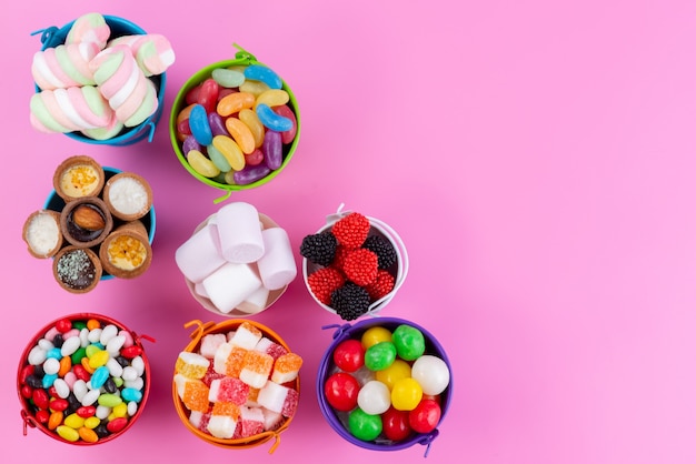 Una vista superior de diferentes dulces como confituras, mermeladas, caramelos dentro de cestas de color rosa, dulce de azúcar