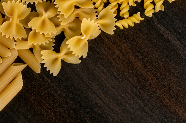 Vista superior de diferentes formas de pasta cruda sobre una superficie de madera