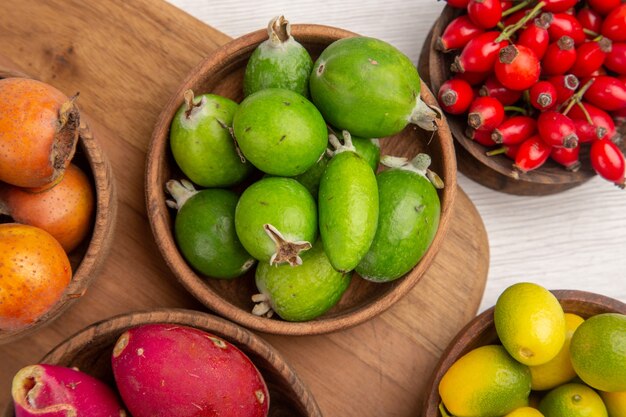 Vista superior de diferentes frutas, bayas de feijoas y otras frutas dentro de las placas en el escritorio blanco color exótico de alimentos maduros