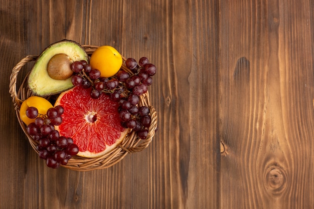 Vista superior de diferentes frutas dentro de la canasta en el escritorio de madera marrón