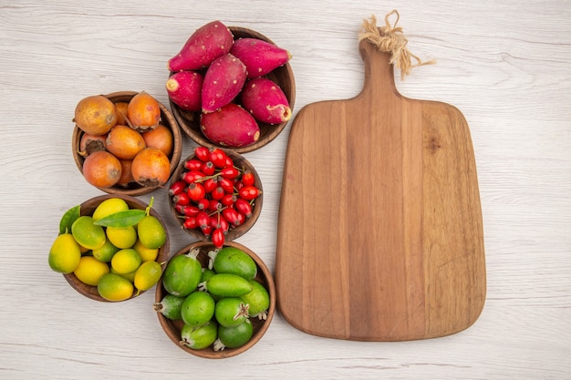 Vista superior de diferentes frutas feijoas y otras frutas dentro de placas sobre fondo blanco, color de salud tropical, árbol de bayas exóticas maduras