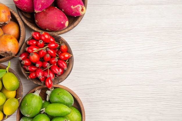 Vista superior de diferentes frutas feijoas y otras frutas dentro de placas sobre fondo blanco, salud tropical, árbol de color de bayas exóticas maduras, lugar libre para texto