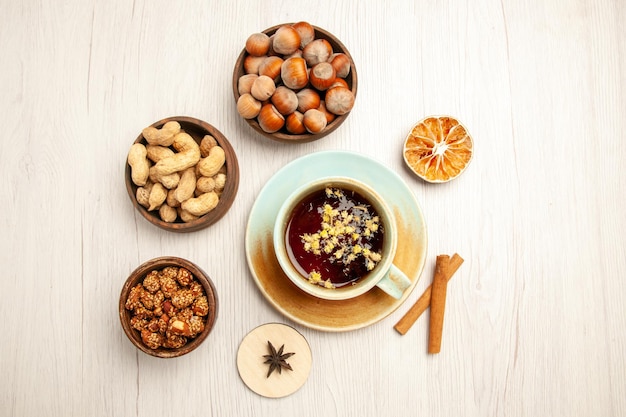 Vista superior de diferentes frutos secos dentro de pequeñas ollas con una taza de té en el escritorio blanco nuez bocadillo nuez avellana