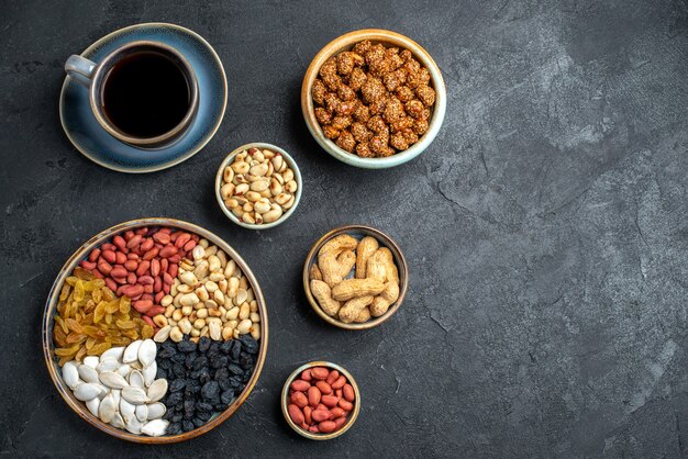 Vista superior de diferentes frutos secos con pasas y una taza de café en el maní de nuez de aperitivo de nuez de escritorio gris oscuro